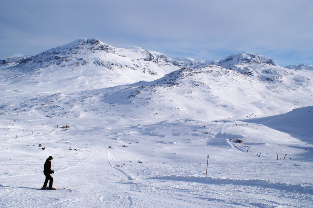 A skier stands at the top of a wide slope in Riksgränsen