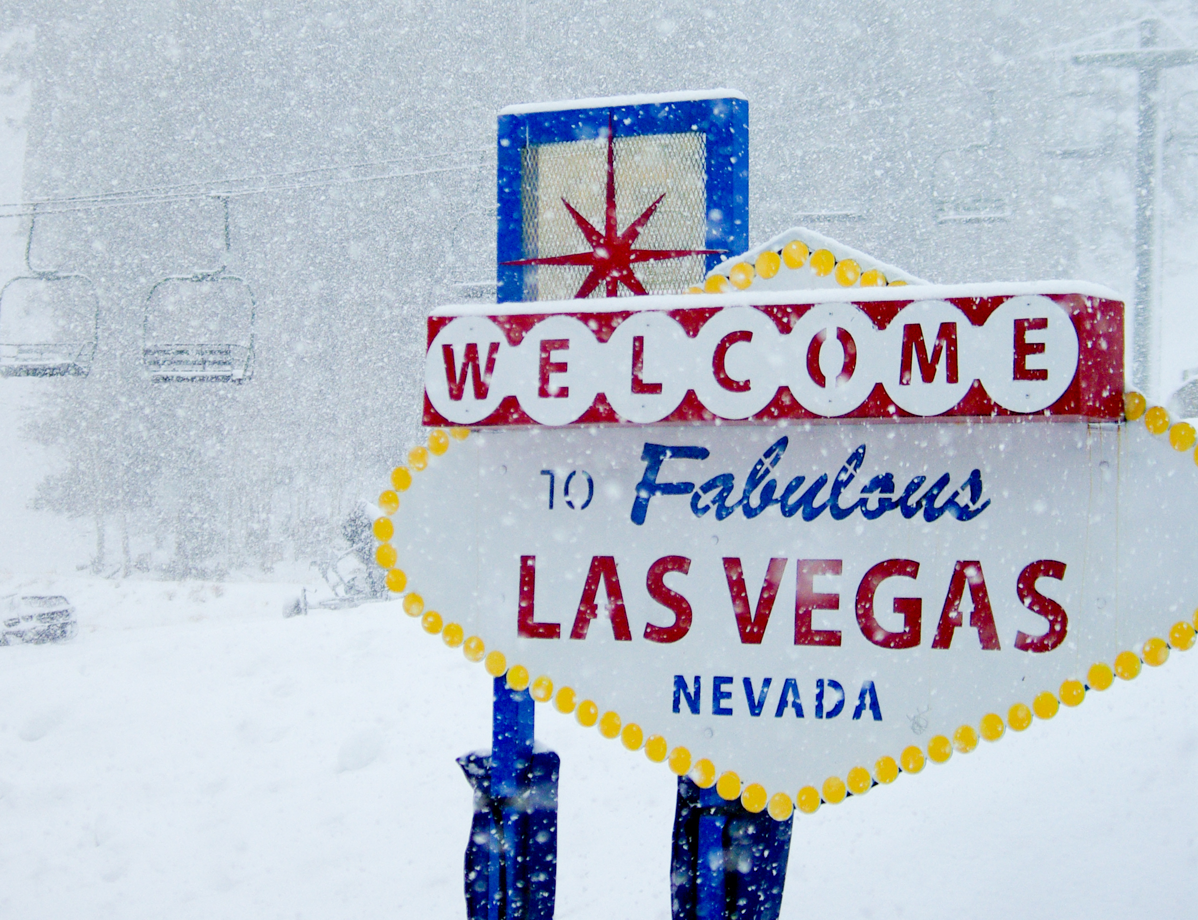 A sign saying "Welcome to Fabulous Las Vegas Nevada" stands in front of a wintry scene with ski lifts in the background and thick snow in the air
