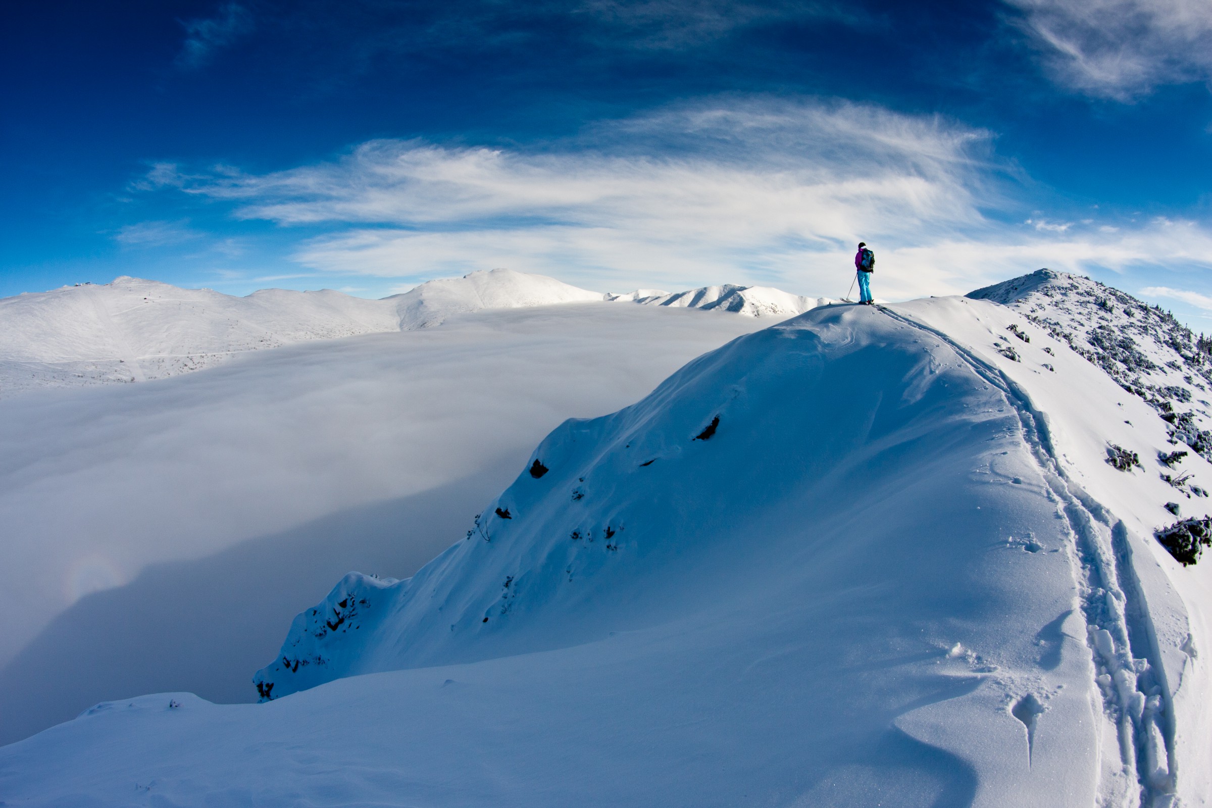 A skier stands on a mountaintop ridge