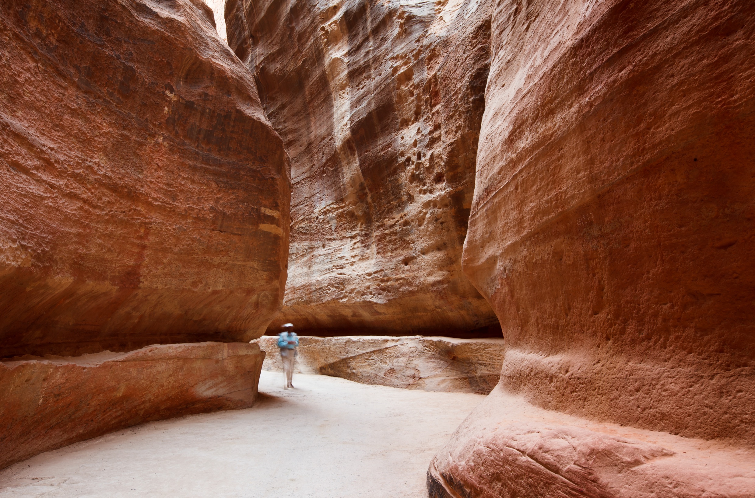 A tourist walks through the wind-blown sandstone walls of the Petra Siq in Jordan