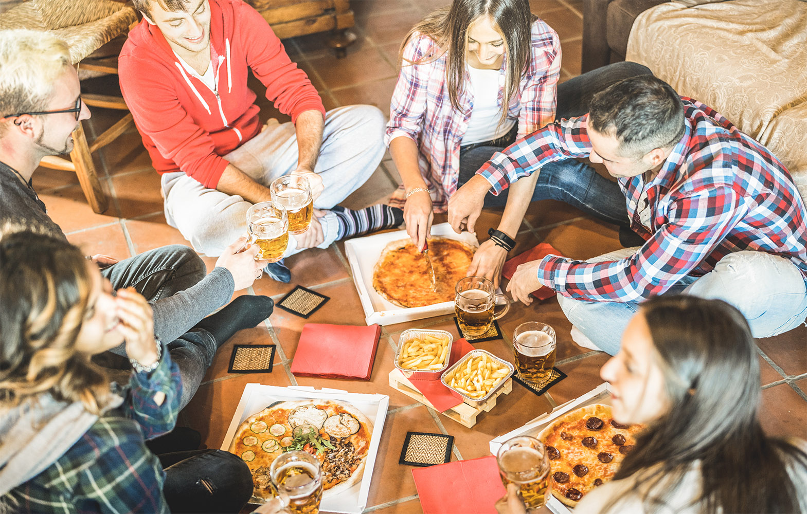 Happy friends eating take away pizza at home after work - Friendship concept with young people enjoying time together and having genuine fun in start up office - Focus on beers and french fries