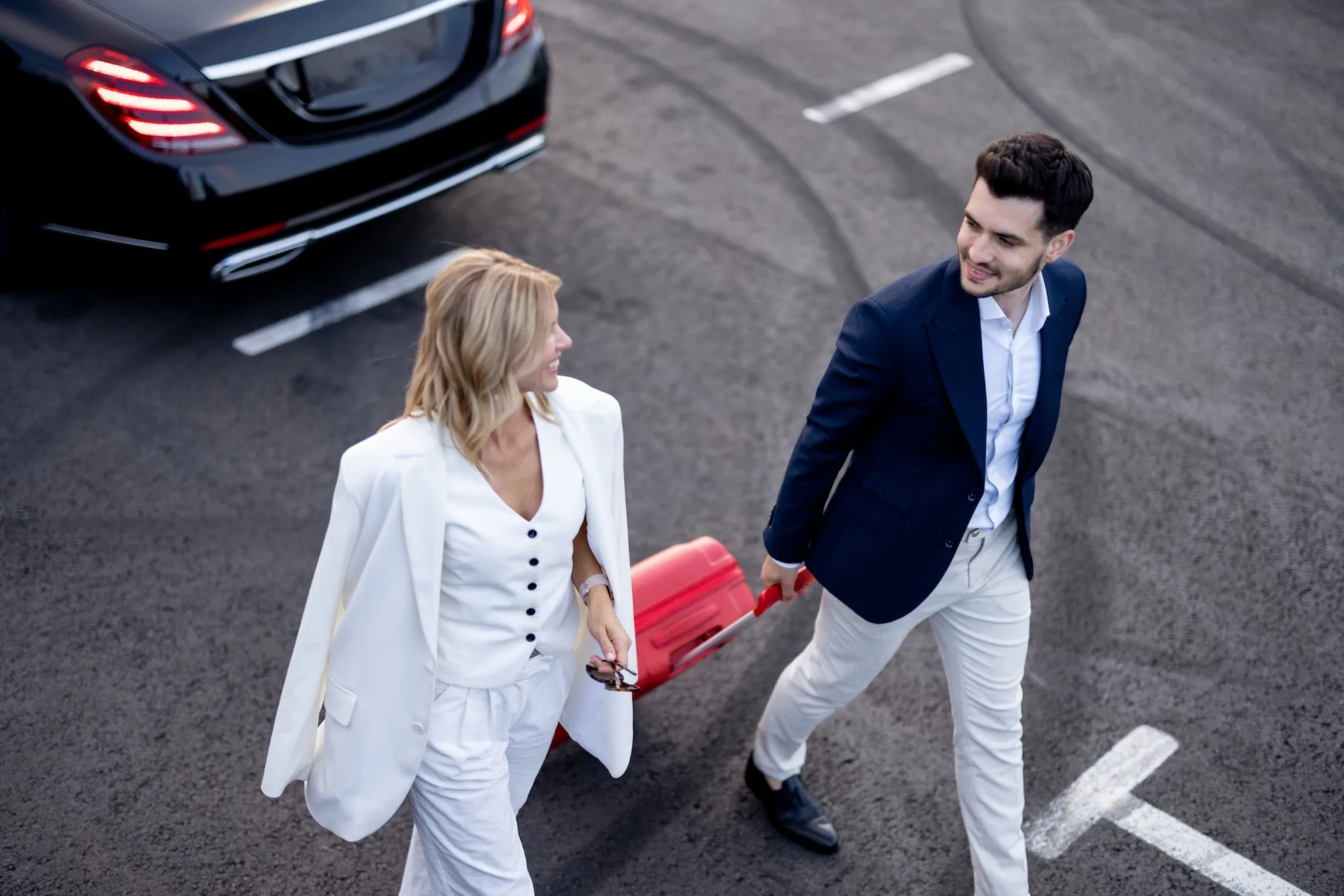 Business,Couple,Walking,With,A,Suitcase,On,Parking,Lot,,Arrived